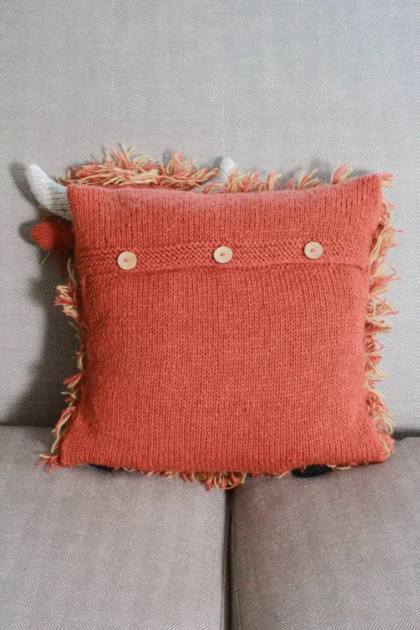 A square-shaped cushion cover featuring a shaggy, textured design in a brown color, with decorative buttons and a fringed edge.