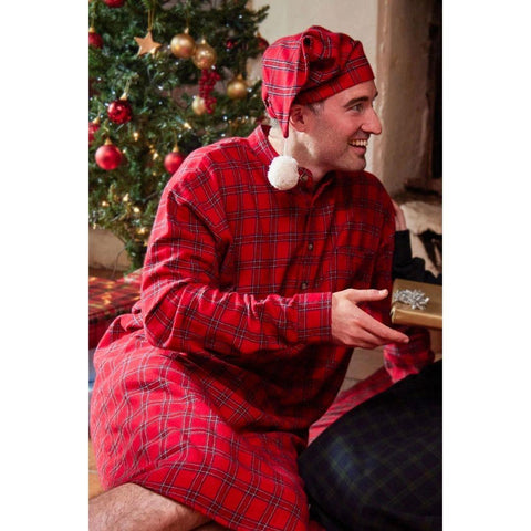 a man wearing red tartan nightshirt and matching sleep cap in front of a christmas tree